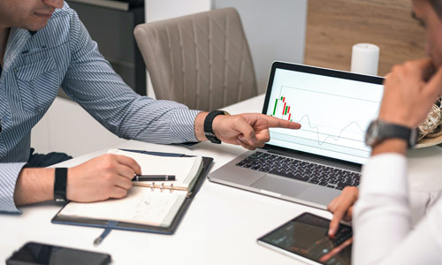 Man Sitting At Desk Discussing Data On A Laptop Screen